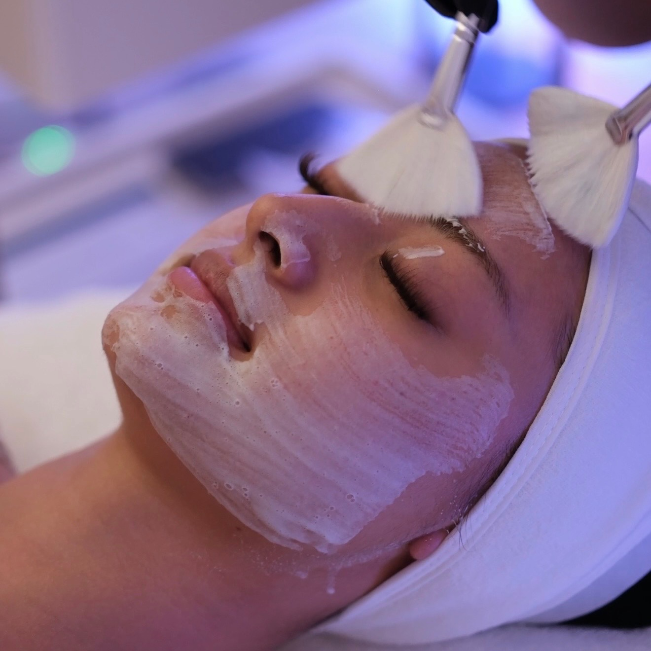 Esthetician cleansing a client's face with fan brushes