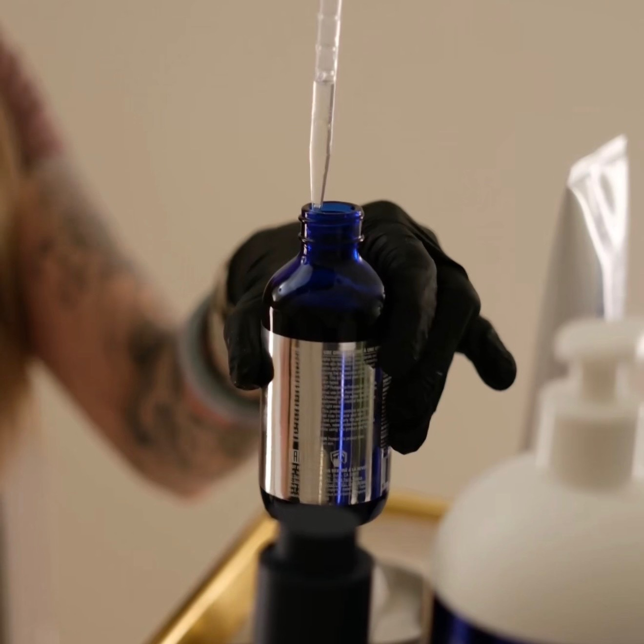 Gloved hand holding a blue bottle with a dropper.