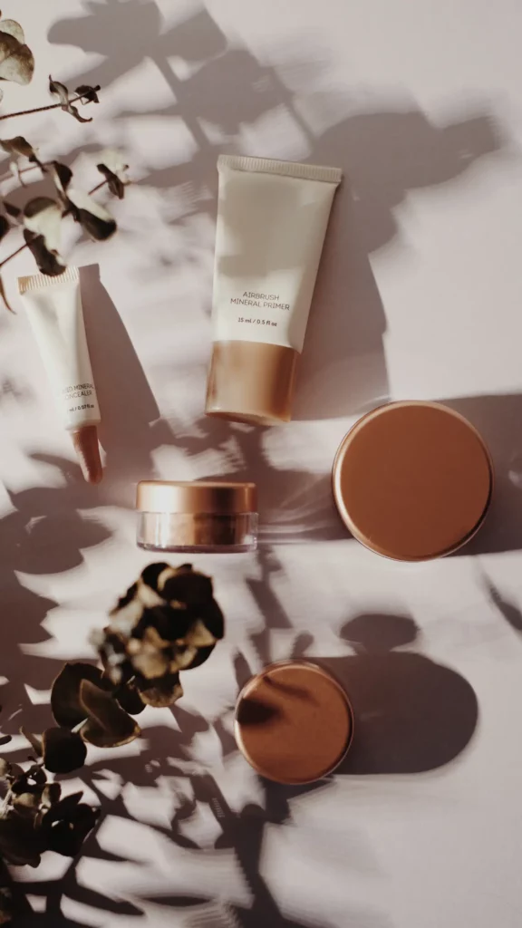 Collection of skincare products artfully arranged against a backdrop with dramatic shadows, cast by natural light filtering through plants.